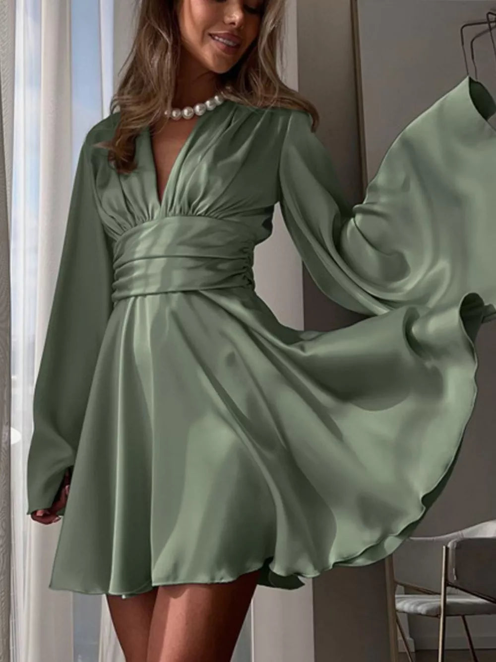 Sage green satin mini dress with deep V-neck, long bell sleeves, and ruched waist detail.