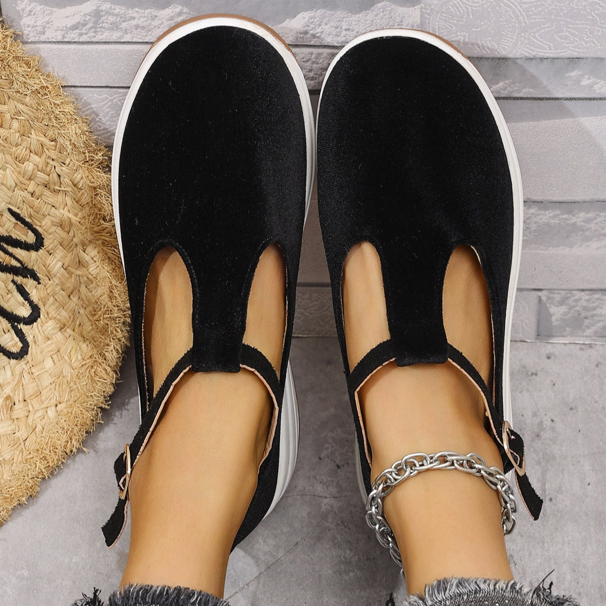 Black T-bar flat slip-ons with adjustable ankle strap and white sole.