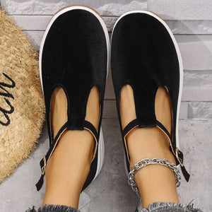 Black T-bar flat slip-ons with adjustable ankle strap and white sole.