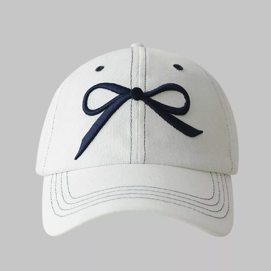 White baseball cap with embroidered dark blue bow accent and contrast stitching