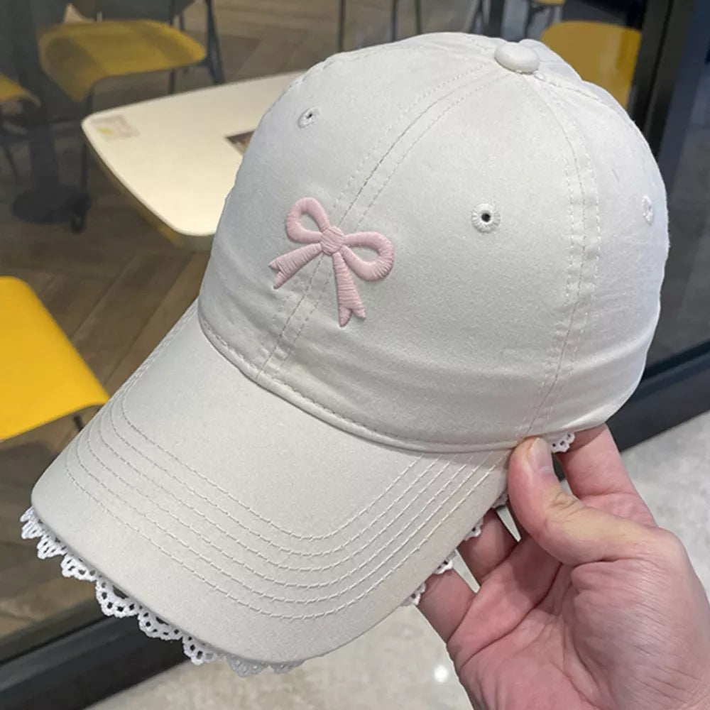 Beige baseball cap with embroidered pink bow and lace trim.