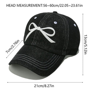 Black denim baseball cap with white embroidered bow detail and contrast stitching.