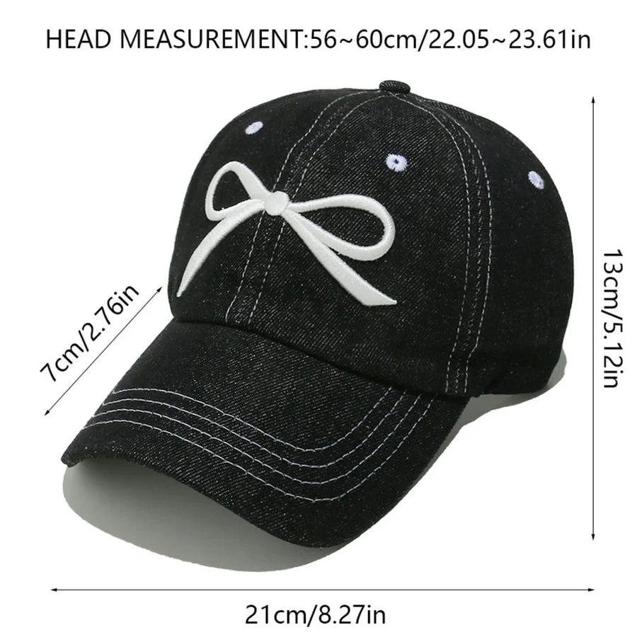 Black denim baseball cap with white embroidered bow detail and contrast stitching.
