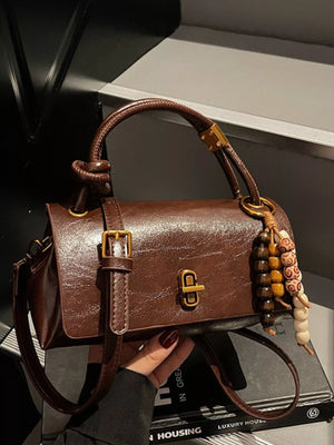 Brown leather crossbody bag with bead charm detail and gold hardware.