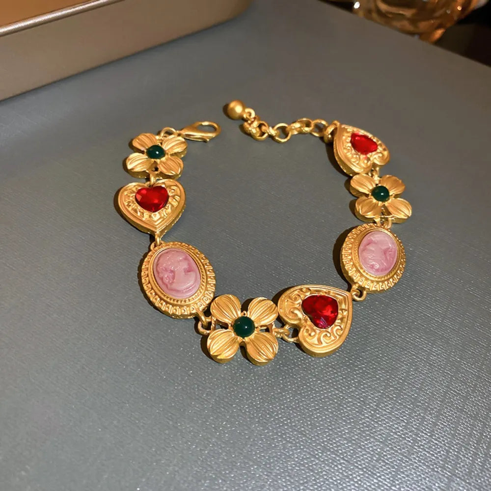 Gold bracelet with cameo, heart, and floral charms with red and green accents