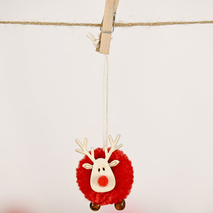 Red pom-pom reindeer Christmas ornament with wooden face and antlers, hanging on a line.