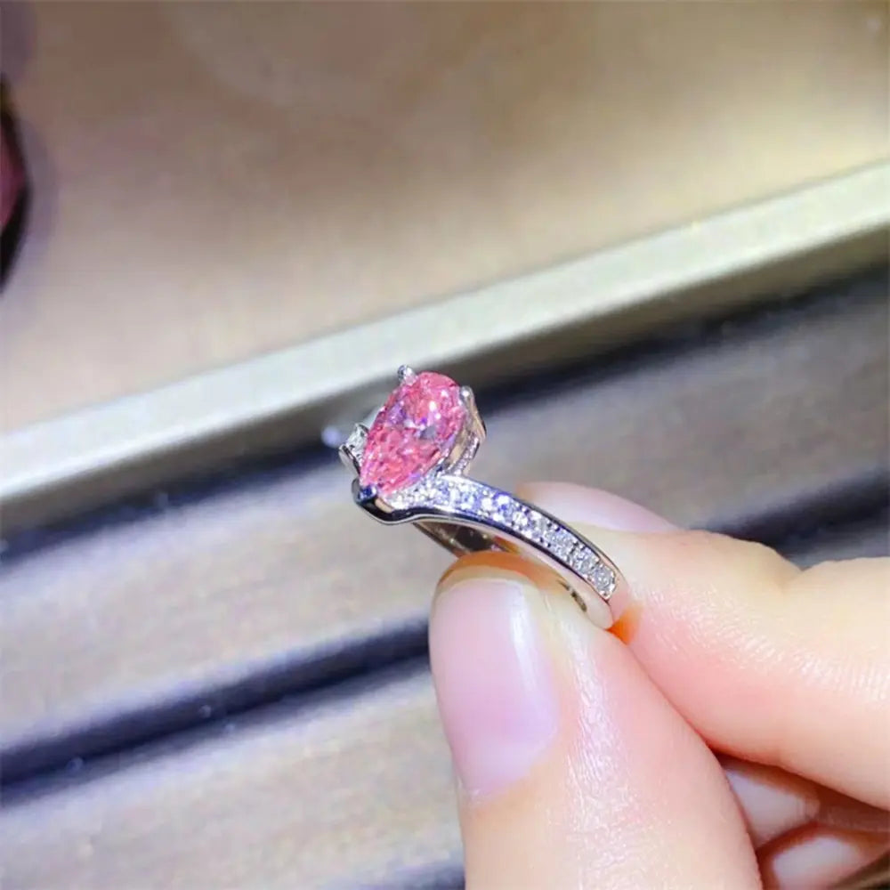 Pink pear-cut moissanite ring with diamond accents on a silver chevron band.
