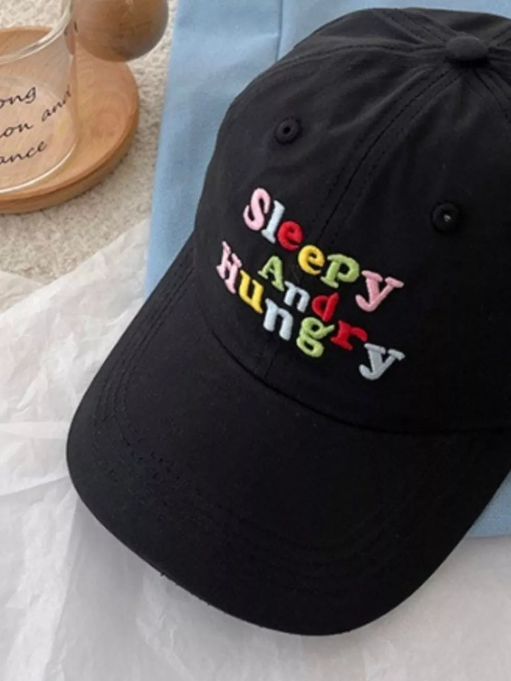 Black baseball cap with colorful embroidered "Sleepy And Hungry" text detail.