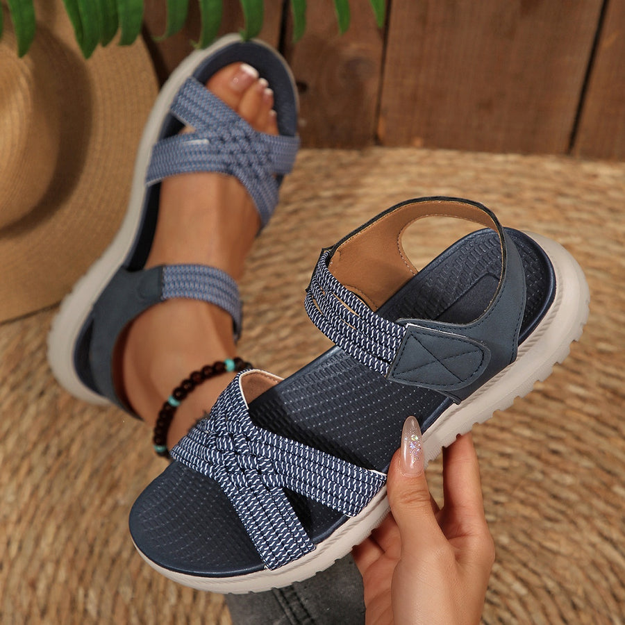 Blue woven strap open-toe flat sandals with adjustable ankle strap and crisscross toe detail.