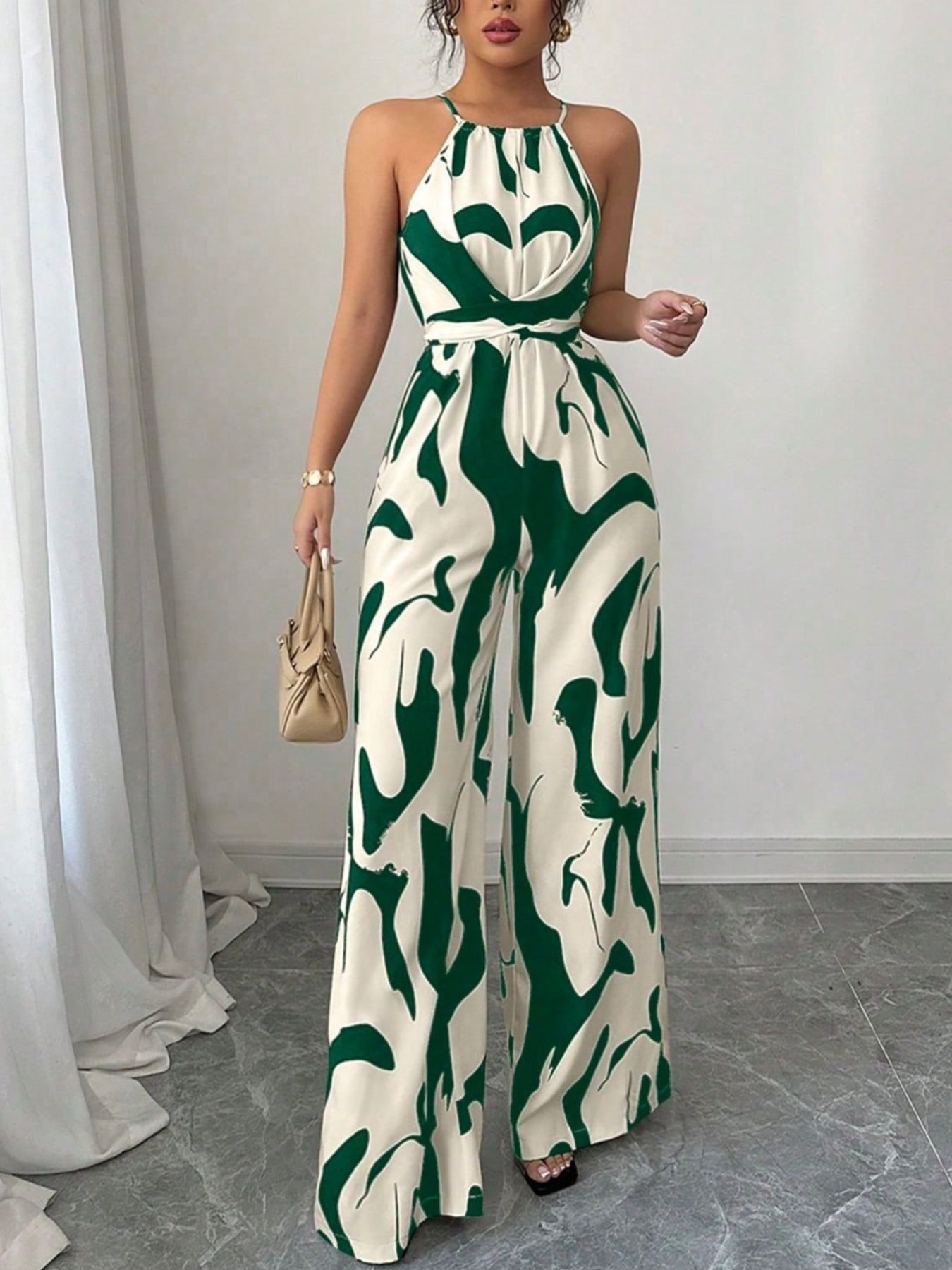 Elegant wide-leg jumpsuit in cream with abstract green print, halter neck, and tie waist.