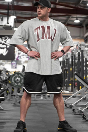 Gray oversized graphic tee with burgundy TMJ logo and athletic shorts.