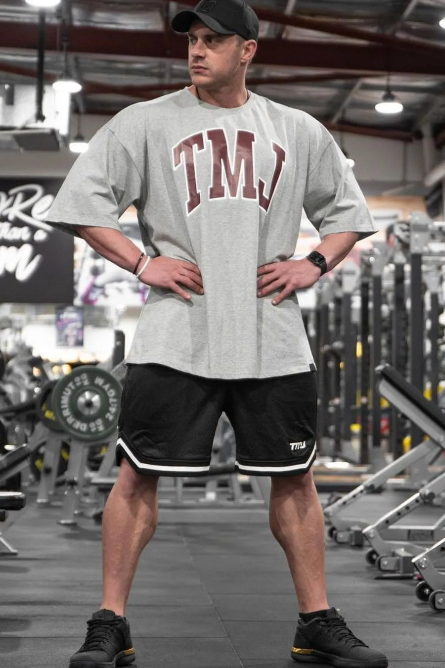 Gray oversized graphic tee with burgundy TMJ logo and athletic shorts.