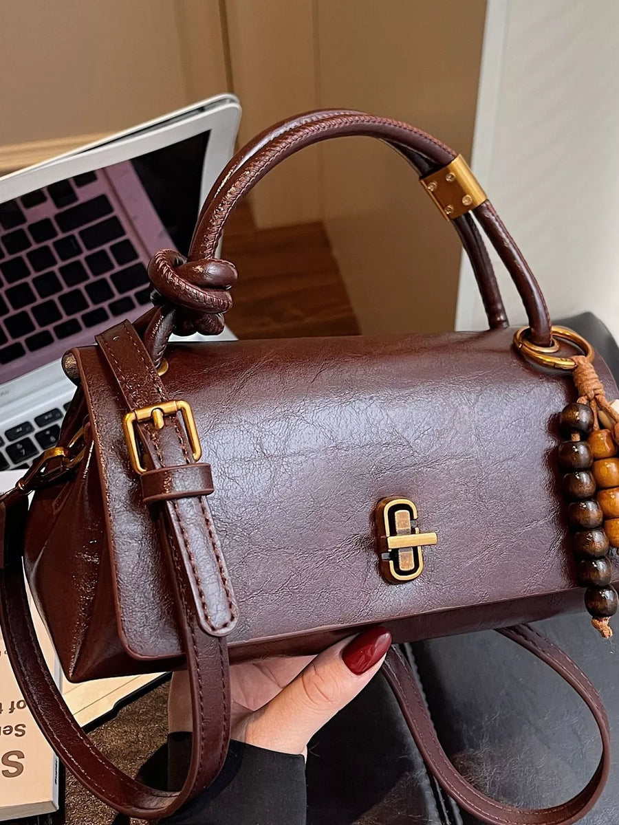 Brown leather crossbody bag with bead charm and gold hardware.
