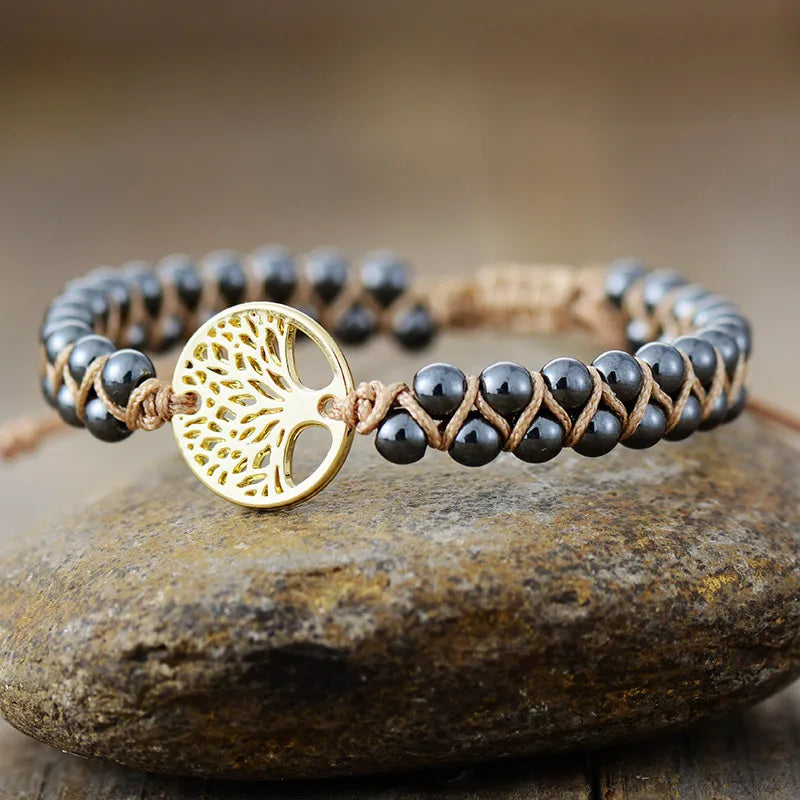 Gold Tree of Life braided bead bracelet with dark gray beads on tan cord.