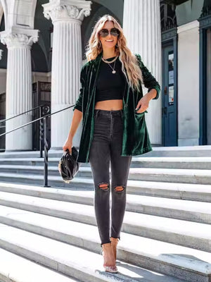 Dark green velvet blazer with drape front and button detail, worn open over a black crop top and ripped jeans.