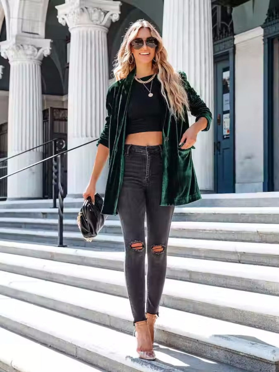 Dark green velvet blazer with drape front and button detail, worn open over a black crop top and ripped jeans.