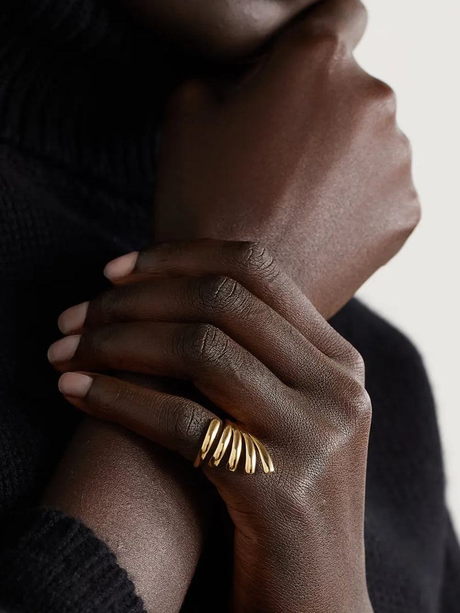 Gold-plated ribbed ring with a sculptural design on a woman's finger.