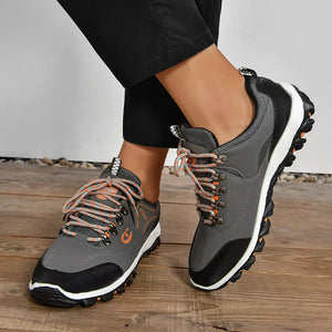 Grey low-top sneakers with patterned orange and grey laces and black accents.