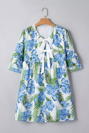 Ruffled mini dress with hydrangea and palm print, featuring a white bow tie neckline and flutter sleeves.