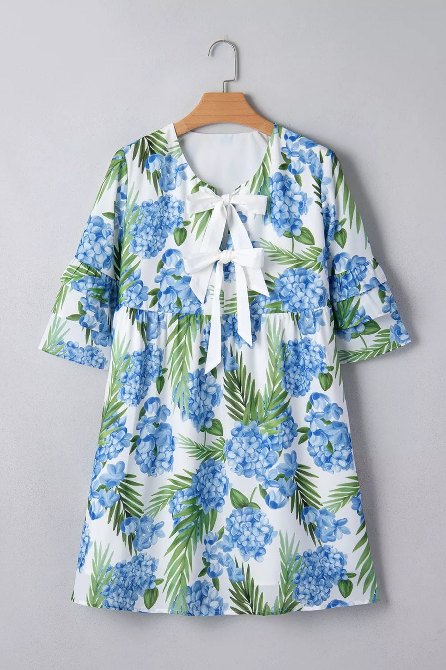 Ruffled mini dress with hydrangea and palm print, featuring a white bow tie neckline and flutter sleeves.