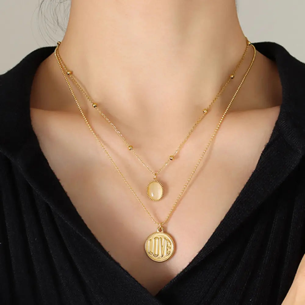 Gold layered necklace with beaded chain, oval charm, and round "love" pendant.