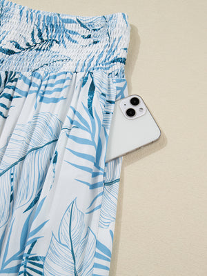 Tropical leaf print wide leg pants with smocked waist and side pocket holding a phone.