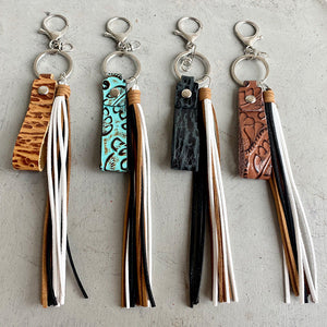 Textured leather tassel keychains in camel, aqua, black, and brown with multi-color fringe.