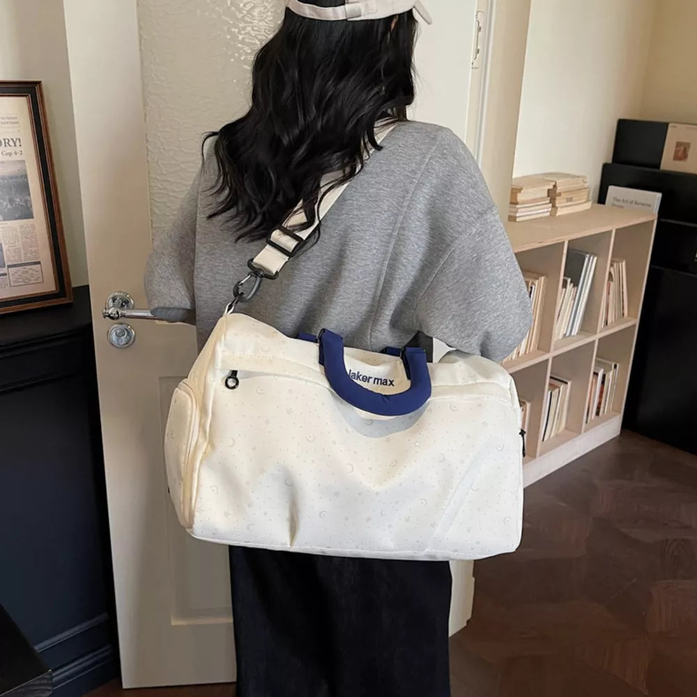Cream white duffel bag with crescent moon and star pattern, blue handles, adjustable strap.