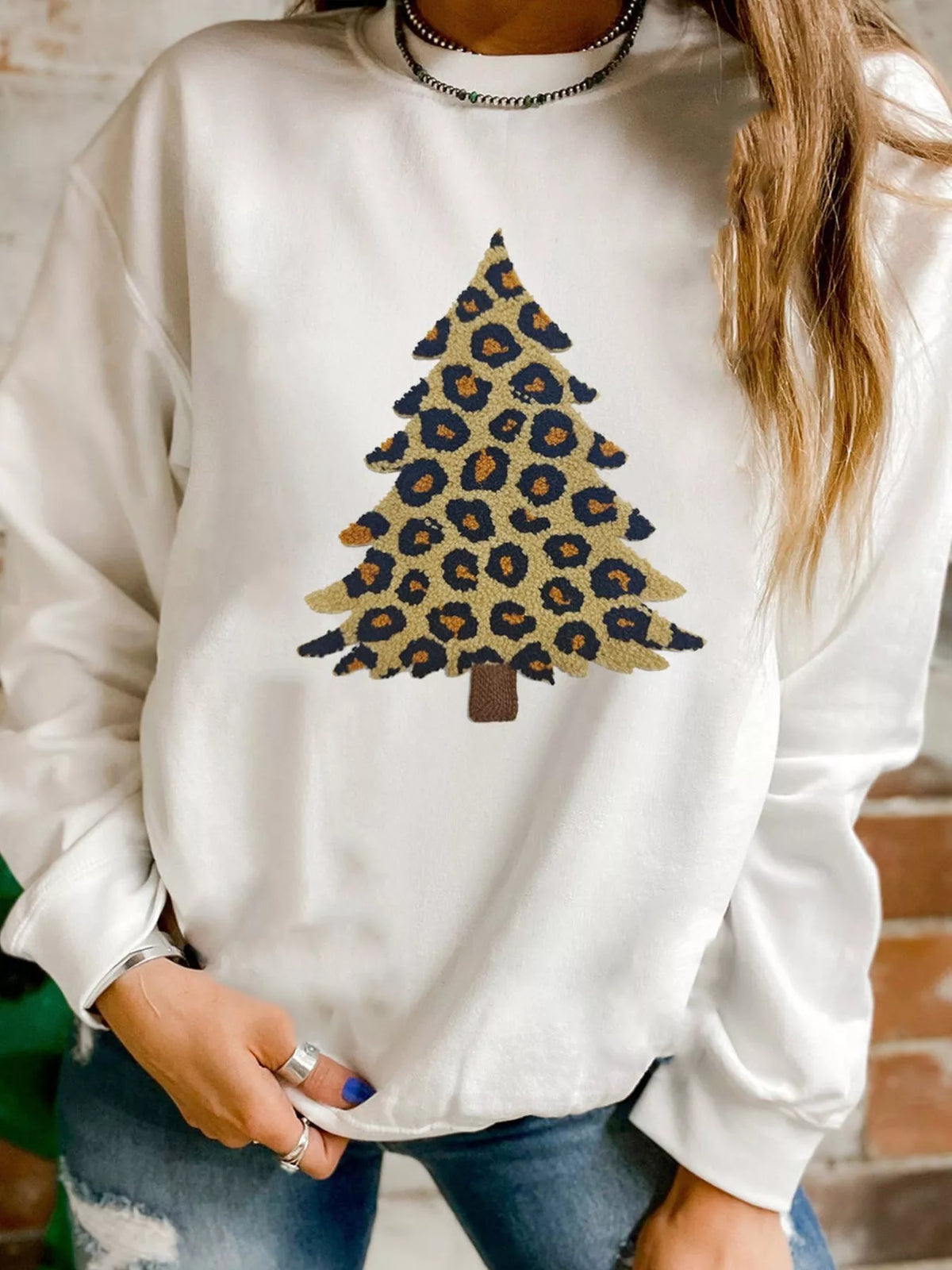 White drop shoulder sweatshirt with a leopard print Christmas tree graphic.