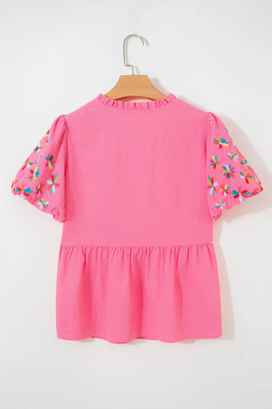 Pink textured peplum blouse with embroidered floral puff sleeves and ruffled neckline.