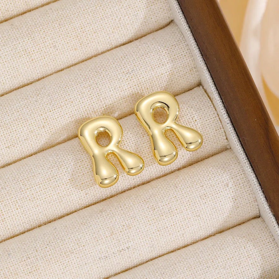 Alphabetical sculpted stud earrings in gold, featuring the letter R.