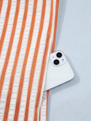 Orange and white striped shift mini dress with a pocket holding a smartphone.