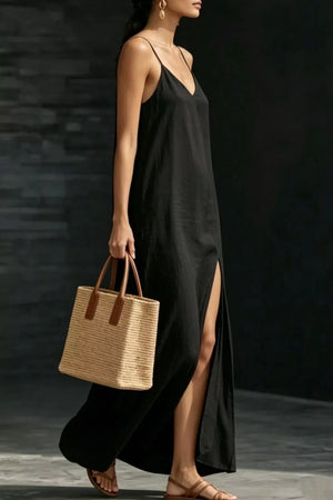 Black V-neck maxi dress with spaghetti straps and a high slit, worn with sandals and a straw tote.
