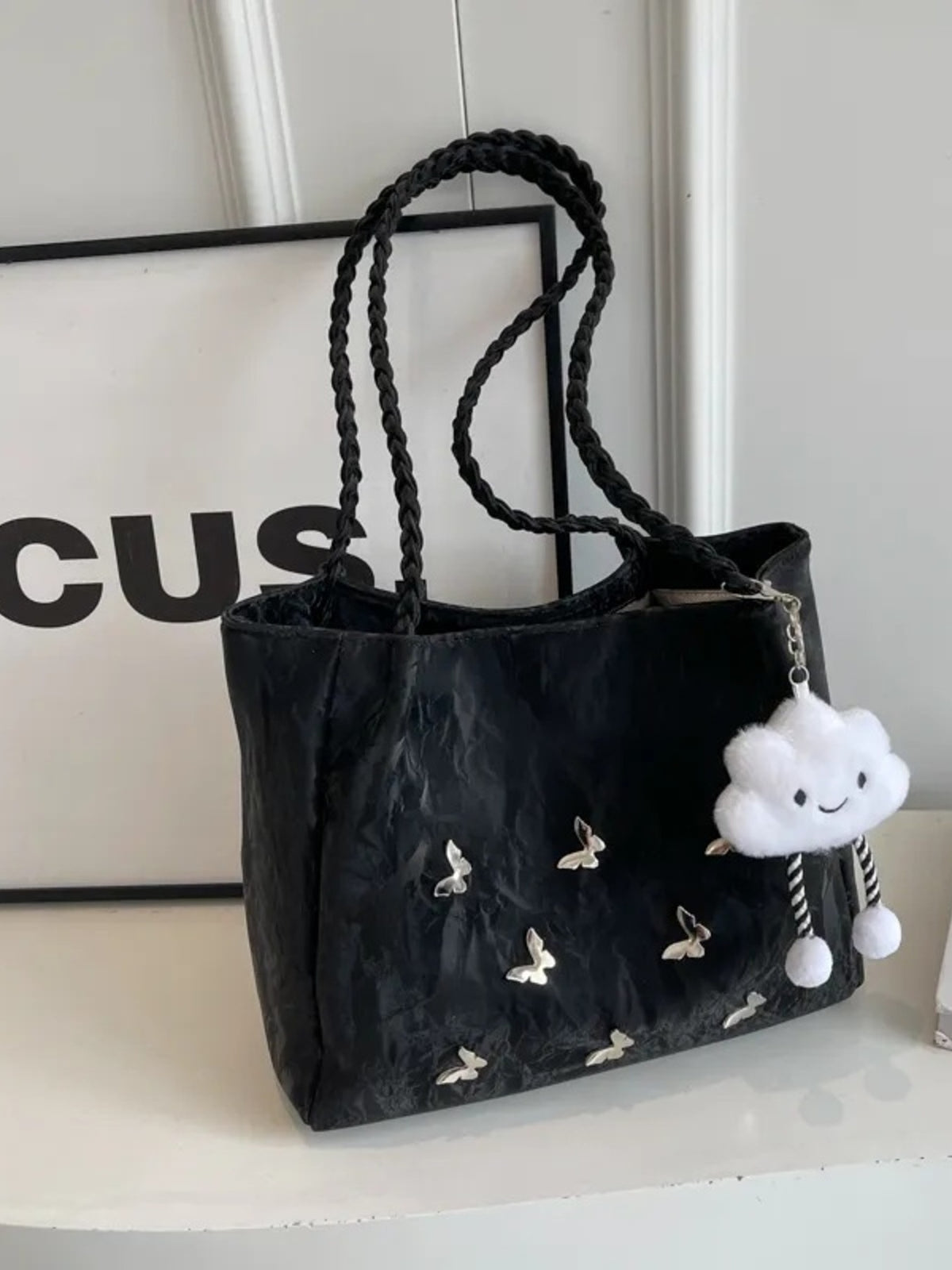 Black shopper bag with braided handles, butterfly details, and cloud charm