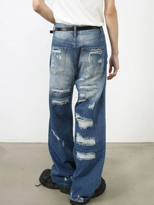Oversized ripped denim jeans in medium wash with raw edge details and distressed accents.