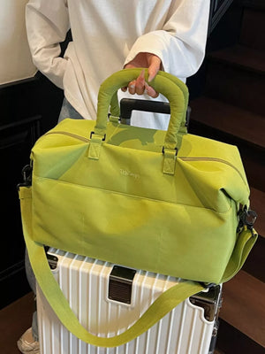 Lime green duffel bag with padded handles and a crossbody strap, resting on a white suitcase.