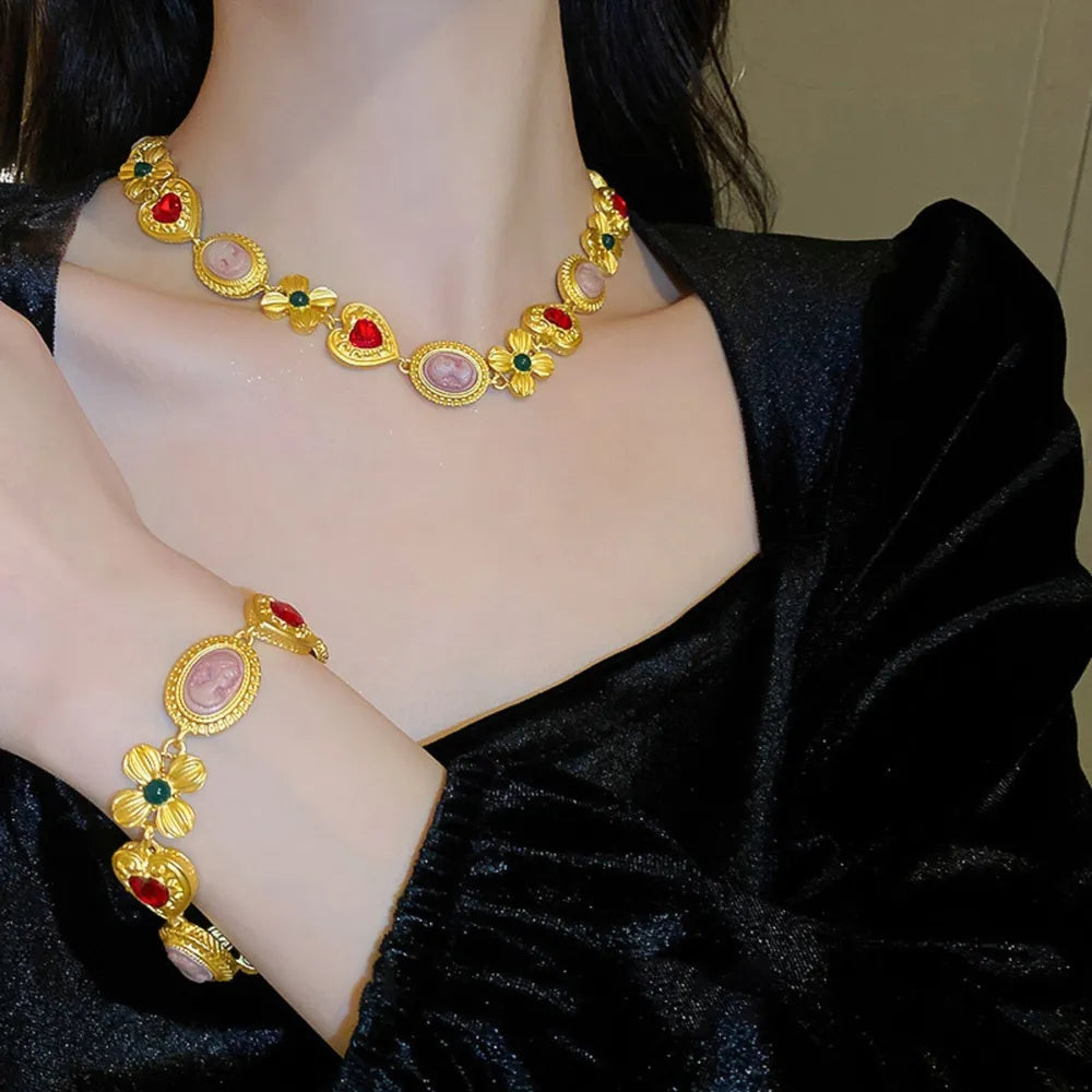 Gold bracelet with cameo, heart, and floral charms with red and green accents.