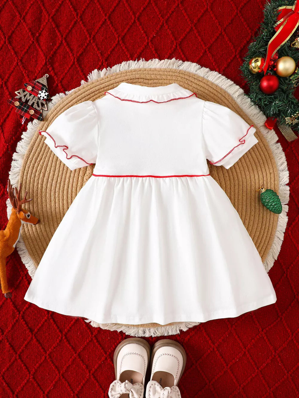 White baby dress with red trim, puff sleeves, and ruffled collar.