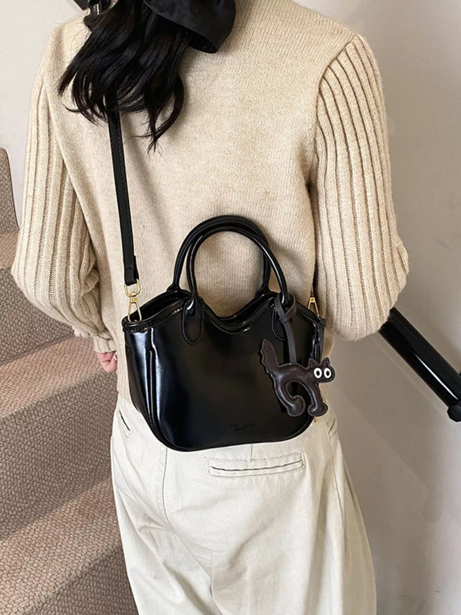 Black patent leather crossbody bag with a cute cat charm and double handles.