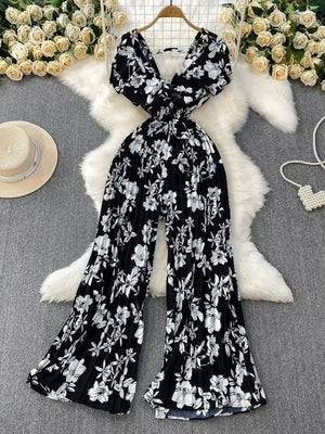 Black floral print wide-leg romper with plunging neckline and pleated wide legs.