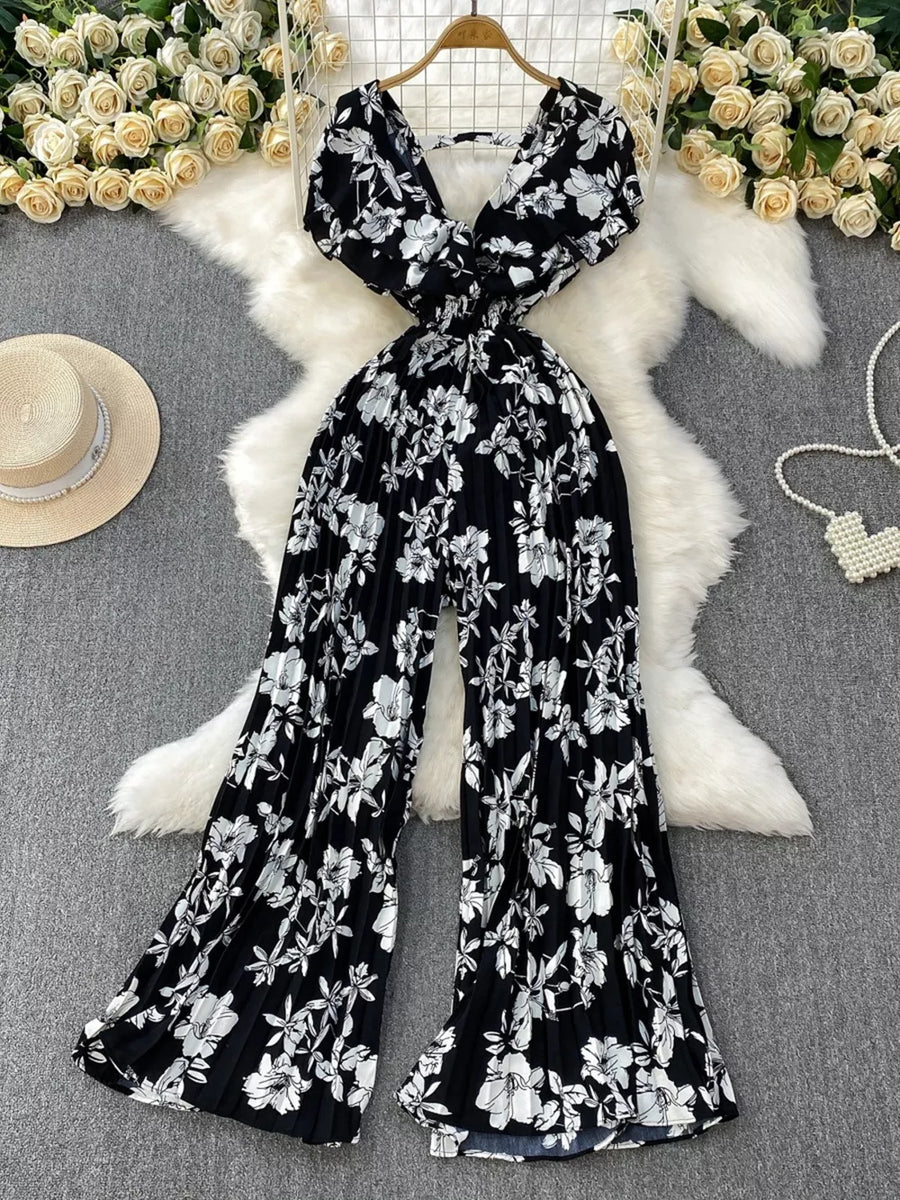 Black floral print wide-leg romper with plunging neckline and pleated wide legs.