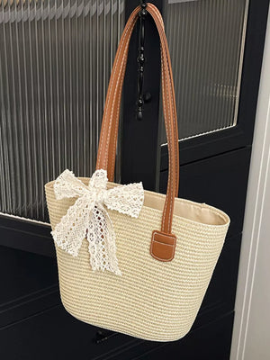 Charming straw shoulder bag in off-white with brown leather straps and lace bow detail.