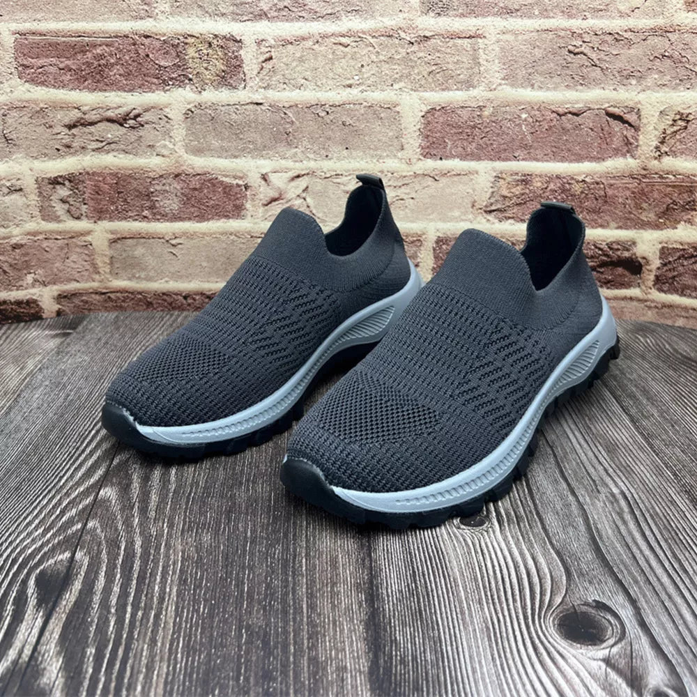 Grey breathable slip-on sneakers with round toe and textured knit upper.