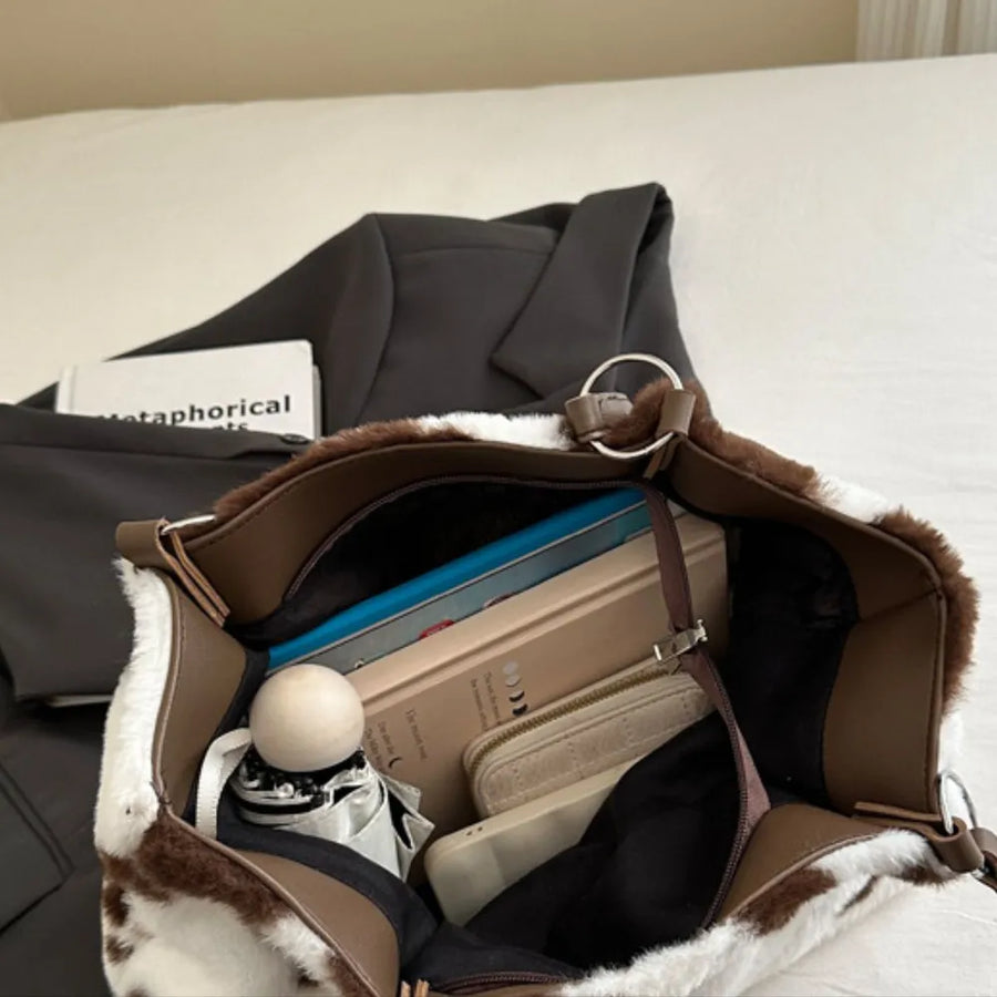 Cowhide print faux fur shopper bag with brown trim and metal ring detail, stuffed with books and accessories.