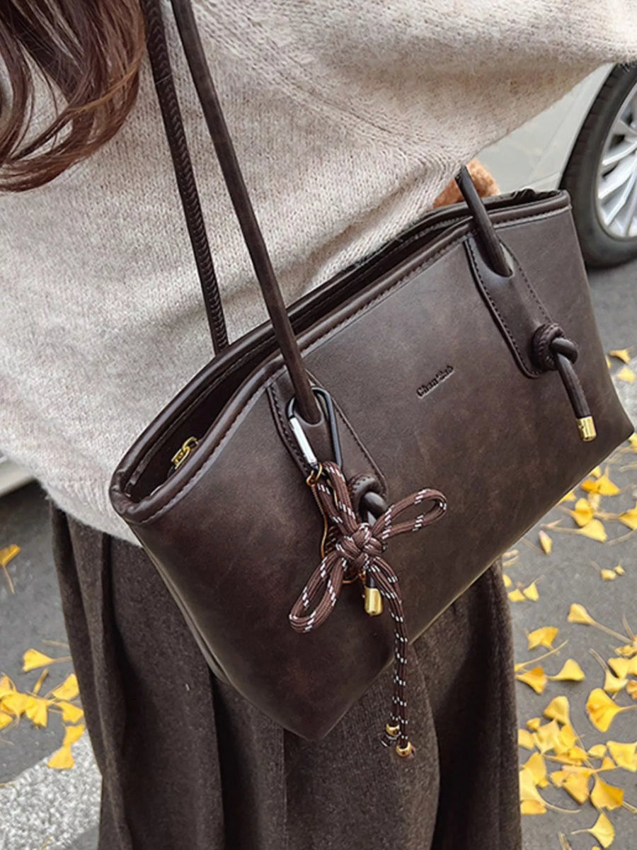 Brown leather shoulder bag with knotted strap detail and gold hardware.