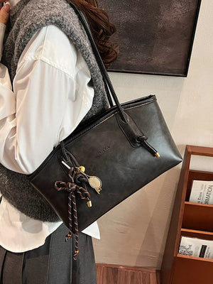 Black leather shoulder bag with decorative charms and knotted strap detail.