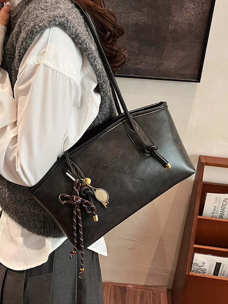 Black leather shoulder bag with decorative charms and knotted strap detail.