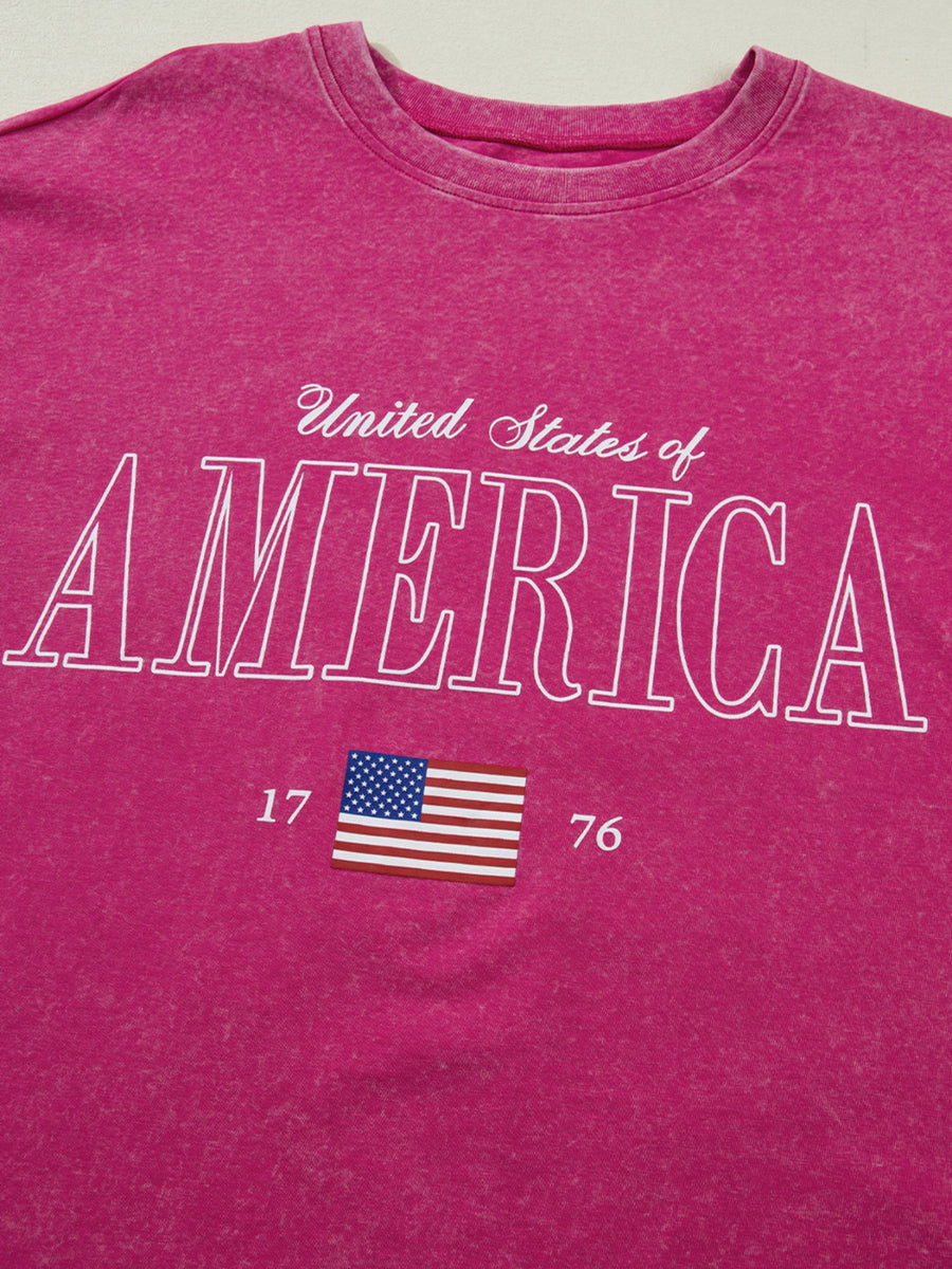 Patriotic graphic cotton t-shirt in pink with "United States of America" text and US flag graphic.