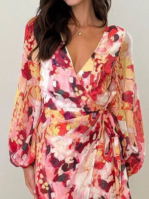 V-neck tie waist dress with abstract floral print in pink, red, and yellow, featuring balloon sleeves.