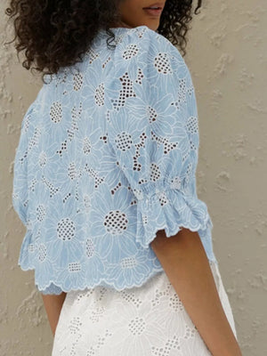 Blue eyelet crop top with white floral embroidery and ruffled sleeves.